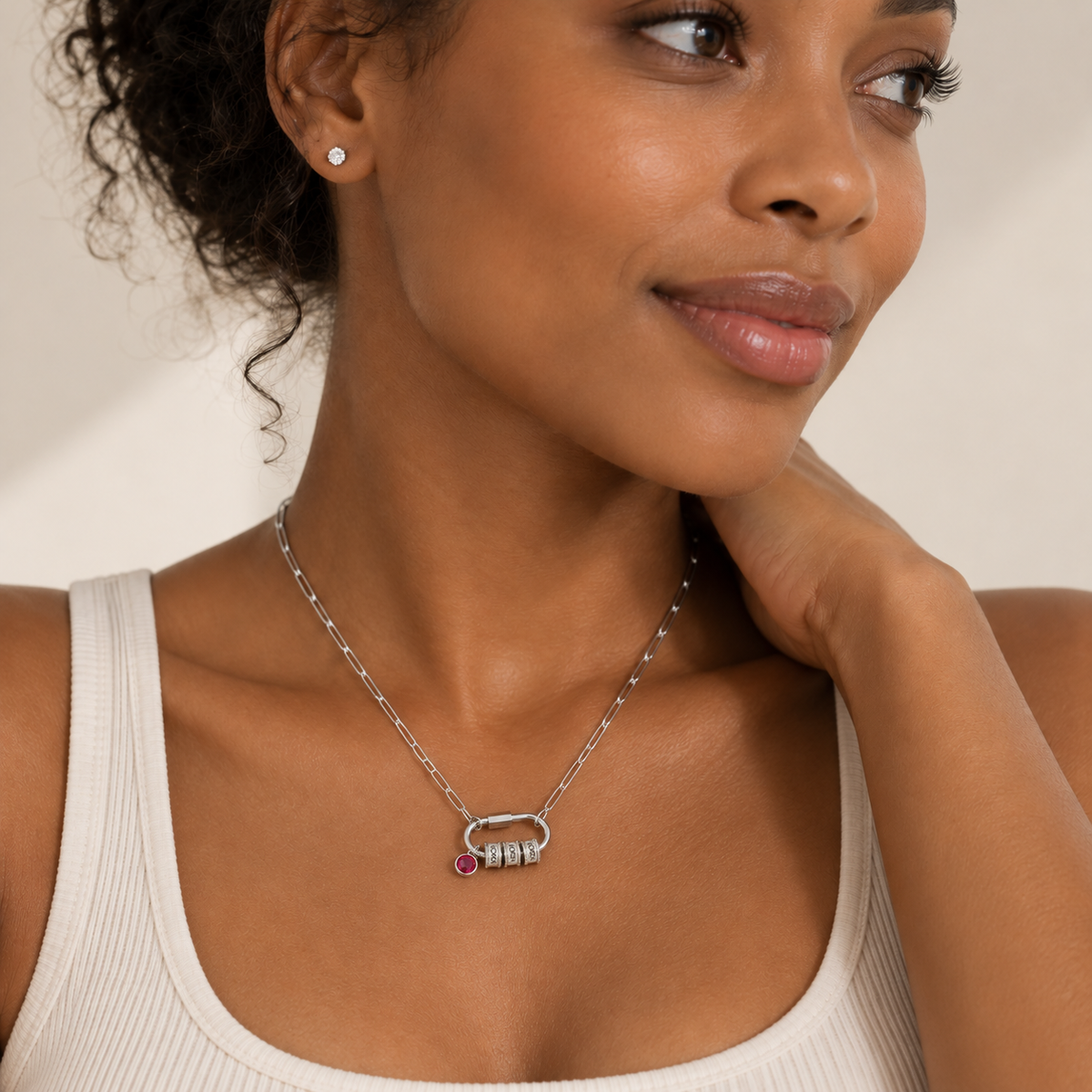 A close-up lifestyle shot of a woman wearing a silver-toned chain necklace with a lock-shaped pendant featuring a small pink gemstone and a barbell detail, paired with a matching stud earring.
