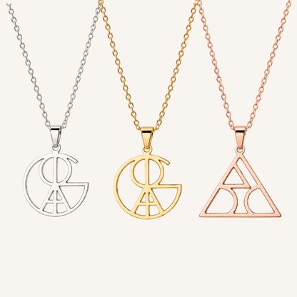 Three necklace pendants on chains against a light warm background: a silver pendant on a silver chain, a gold pendant on a gold chain, and a rose gold pendant on a rose gold chain. Each pendant features an open geometric monogram-style design.